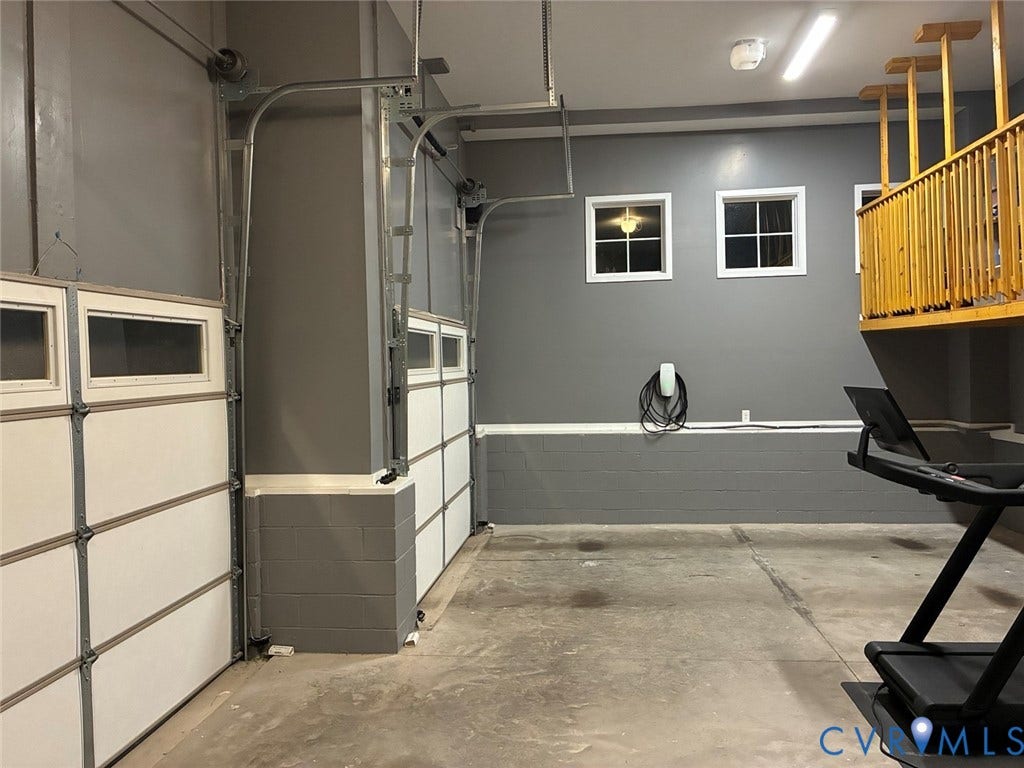 4600 Otter Court, Moseley, VA 23120 Spacious garage featuring two overhead doors with upper window panels, a concrete floor, and an EV charging station