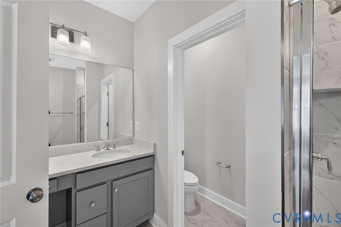 1509 Moore Street, #B, Richmond, VA 23220 Bathroom featuring a gray vanity with a light-toned countertop, a large wall-mounted mirror, a two-light vanity fixture, and a glass-enclosed shower with tiled walls