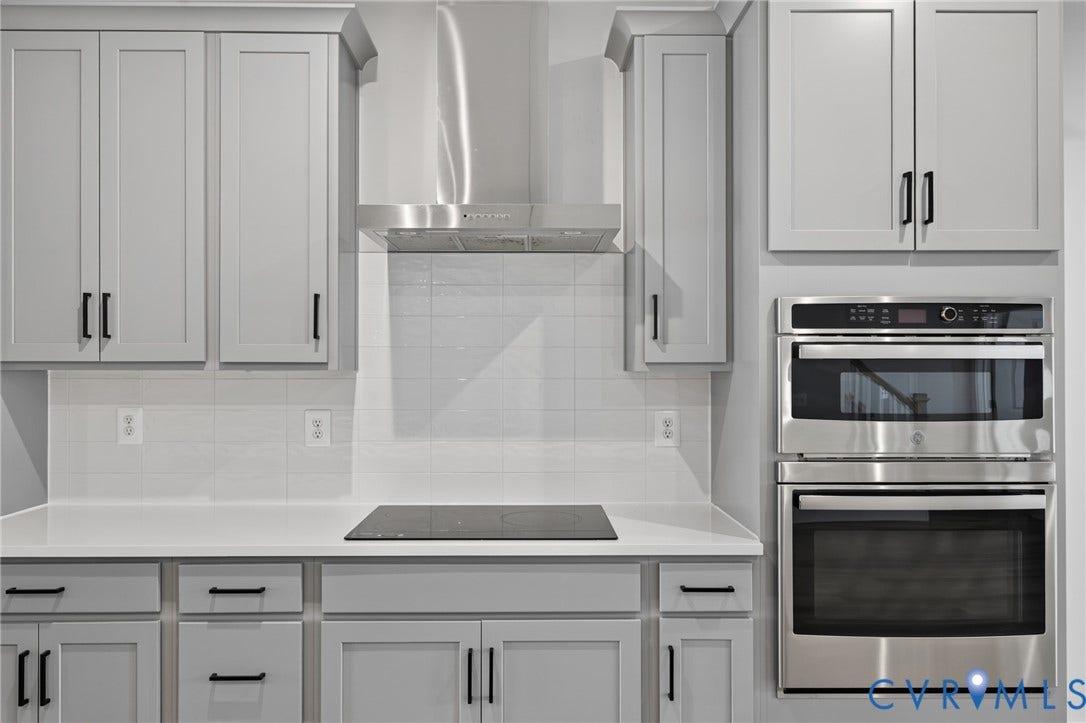 1509 Moore Street, #B, Richmond, VA 23220 Light gray cabinetry with black hardware, white subway tile backsplash, stainless steel range hood, built-in double oven, and integrated cooktop