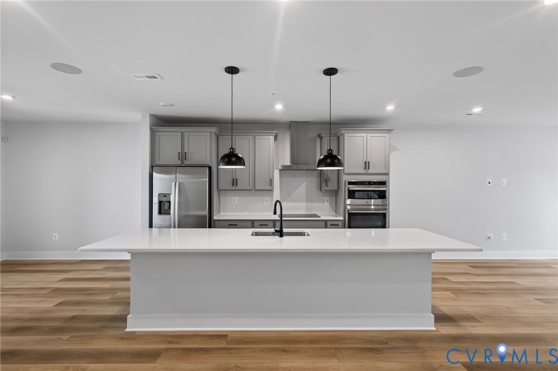 1509 Moore Street, #B, Richmond, VA 23220 Expansive kitchen island with a built-in sink and two pendant lights, wood-finish flooring, stainless steel appliances, and shaker-style cabinetry