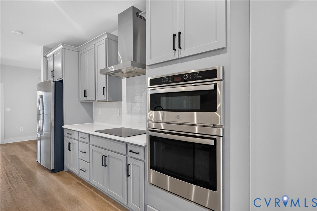 1509 Moore Street, #B, Richmond, VA 23220 White shaker cabinetry, stainless steel appliances, solid surface countertops, tile backsplash, and wood-finish flooring