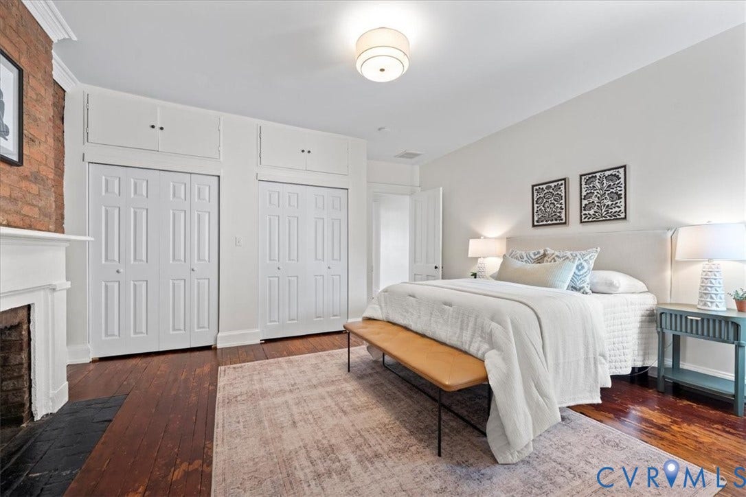 2510 E Leigh Street, Church Hill, Richmond, VA 23223 Exposed brick fireplace with a white mantel, wood-finish flooring, and white bi-fold closet doors with upper cabinetry