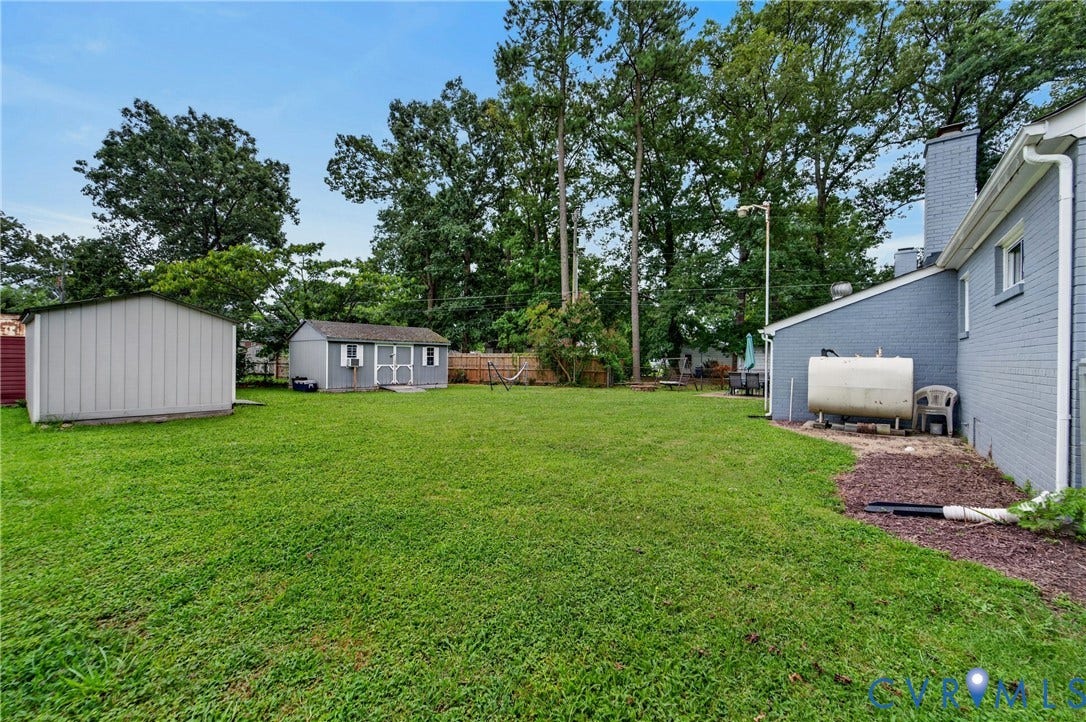 3401 Austin Avenue, Brentwood, Henrico, VA 23222 Expansive green lawn with two detached storage sheds, mature trees, and partial exterior of a gray brick residence