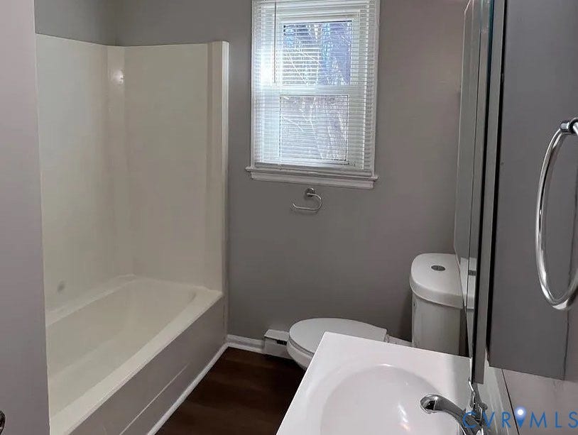 20507 Hickory Court, South Chesterfield, VA 23803 Bathroom featuring a white bathtub and shower surround, a single vanity with an integrated sink, a toilet, a window with blinds, and wood-finish flooring
