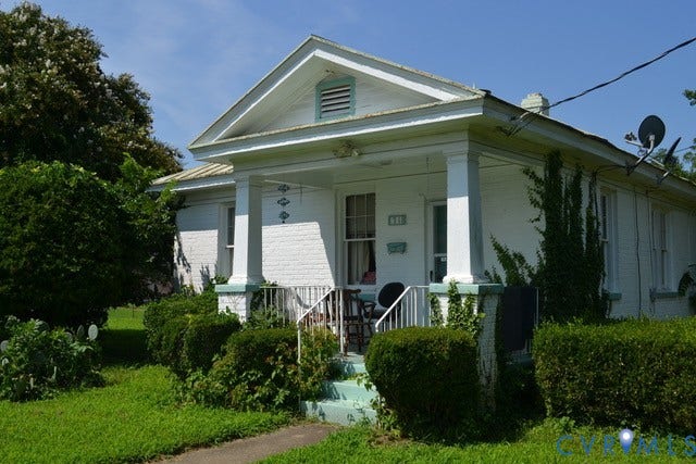 White brick exterior with a columned front porch, gabled roofline, and established landscaping