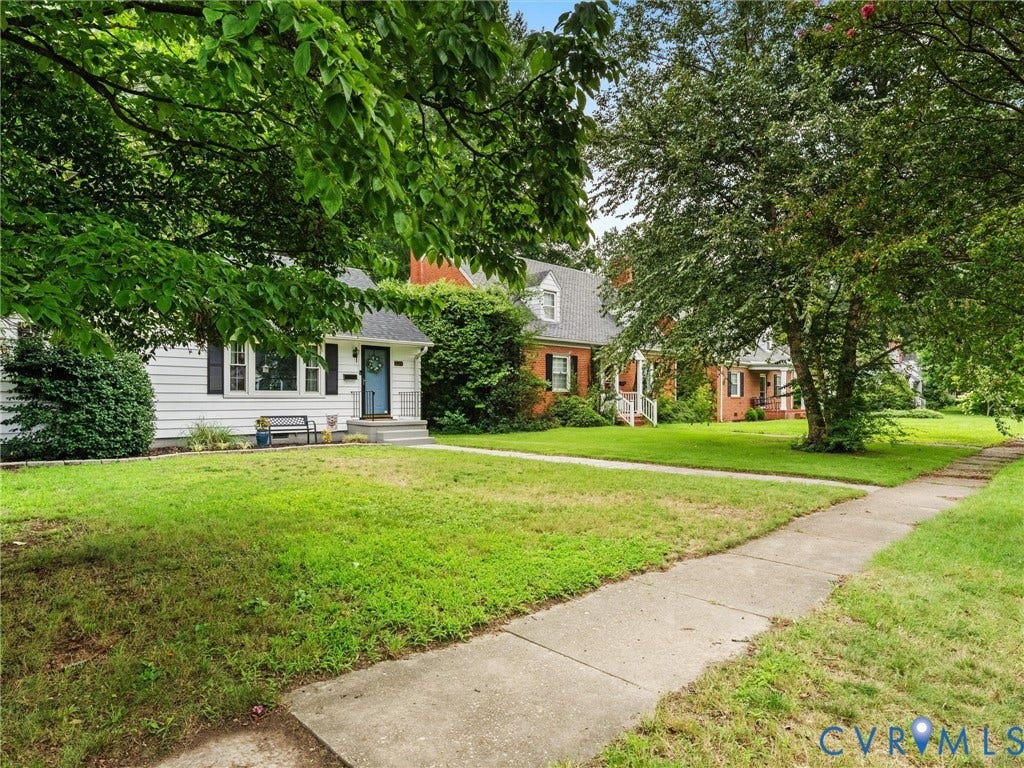 5023 E Seminary Avenue, Richmond, VA 23227 White clapboard siding with black louvered shutters, a vibrant blue front door, and a concrete walkway