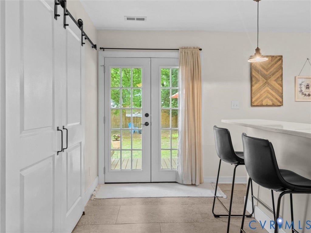 5023 E Seminary Avenue, Richmond, VA 23227 Double French patio doors with grid-patterned glass open to an exterior area, featuring a white barn door with black hardware, ceramic tile flooring, and a peninsula countertop with an overhead pendant light