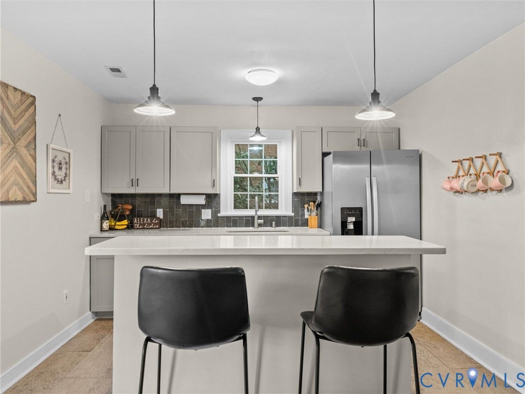 5023 E Seminary Avenue, Richmond, VA 23227 Kitchen featuring an island with seating, stainless steel refrigerator, gray cabinetry, dark subway tile backsplash, and light wood-finish flooring