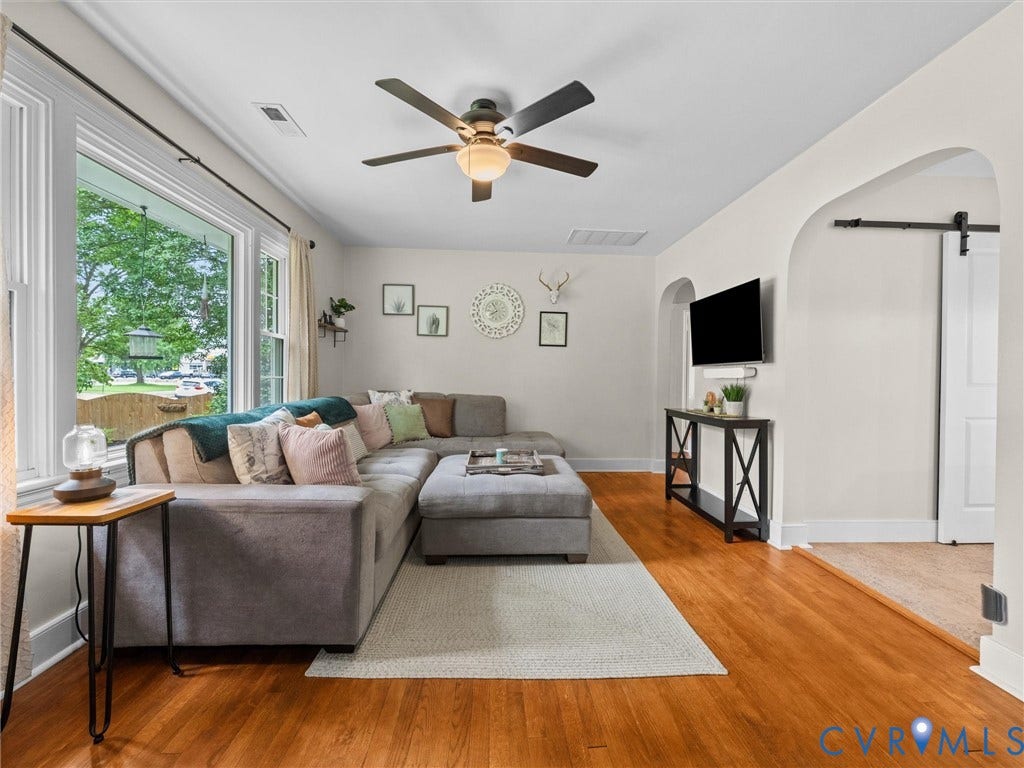 5023 E Seminary Avenue, Richmond, VA 23227 Spacious living area featuring expansive windows, wood-finish flooring, a ceiling fan with integrated lighting, an arched entryway, and a barn door on a black metal track