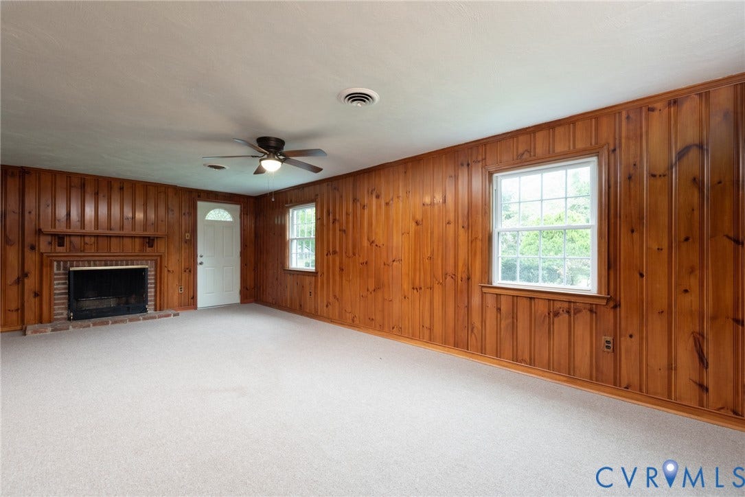 2519 Woodmont Drive, Woodmont, Chesterfield, VA 23235 Spacious room featuring wood paneling, a brick fireplace with a wood mantel, and light-colored carpeting