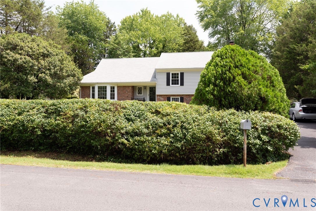 2519 Woodmont Drive, Woodmont, Chesterfield, VA 23235 Hedged frontage with a split-level residence featuring brick and siding facades, a white shingle roof, and dark window shutters
