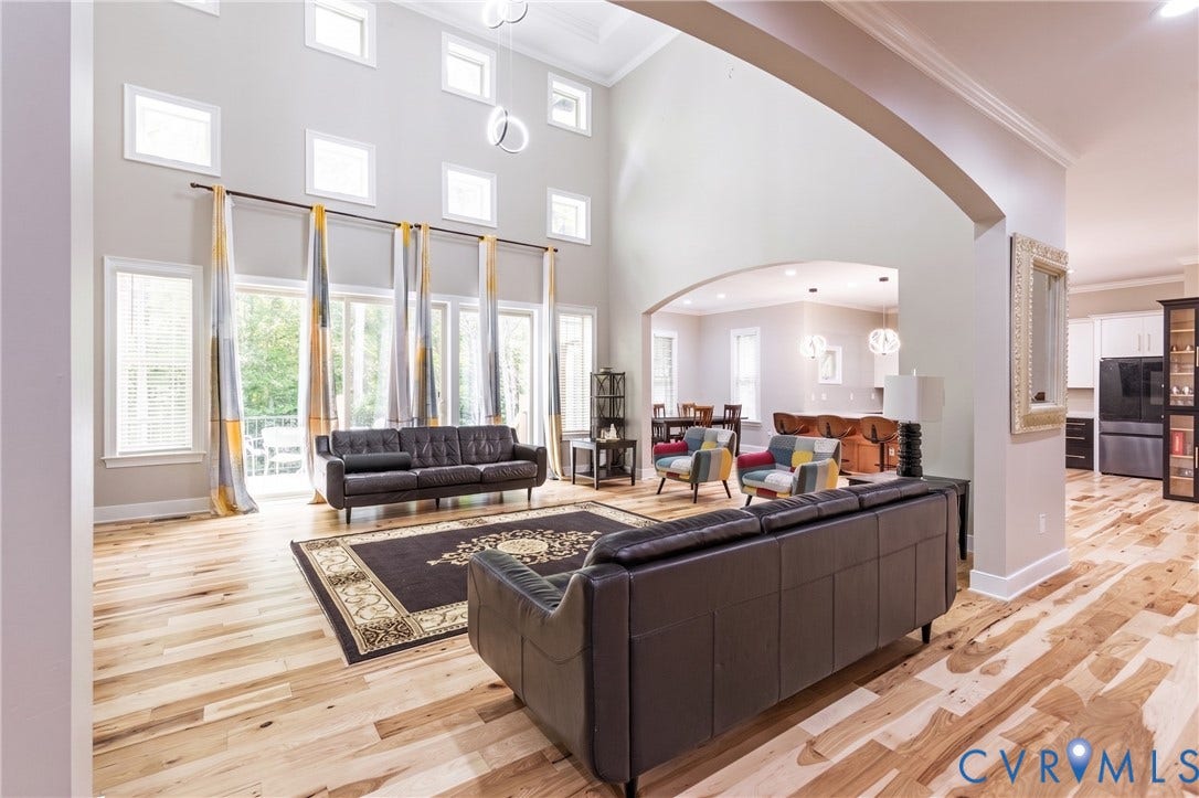 12554 Kain Road, Glen Allen, VA 23059 Two-story living area with high ceilings, multiple large windows, natural wood-finish flooring, and an arched entry to an additional space