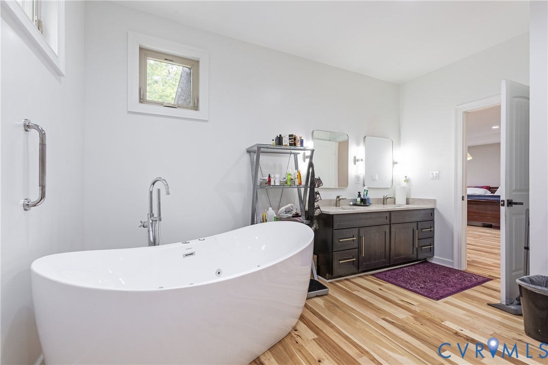 12554 Kain Road, Glen Allen, VA 23059 Spa-inspired primary bathroom featuring a freestanding oval soaking tub, dual-sink vanity with dark cabinetry and integrated storage, wood-finish flooring, and chrome fixtures throughout