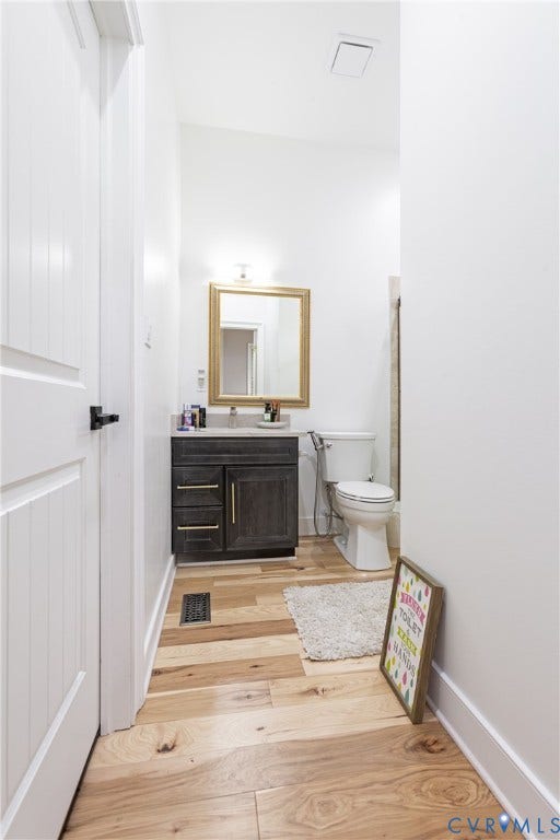 12554 Kain Road, Glen Allen, VA 23059 Renovated bathroom featuring a dark wood vanity with multiple drawers, gold-framed mirror, wood-finish flooring throughout, white subway tile wainscoting, and modern fixtures including a ceramic toilet and chrome hardware