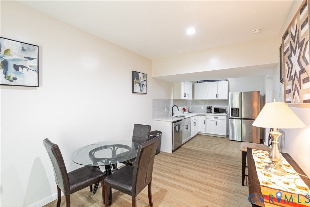 12554 Kain Road, Glen Allen, VA 23059 Open-concept living and kitchen area featuring wood-finish flooring throughout, a round glass dining table with seating for four, stainless steel appliances, white cabinetry with hardware accents, and recessed ceiling lighting