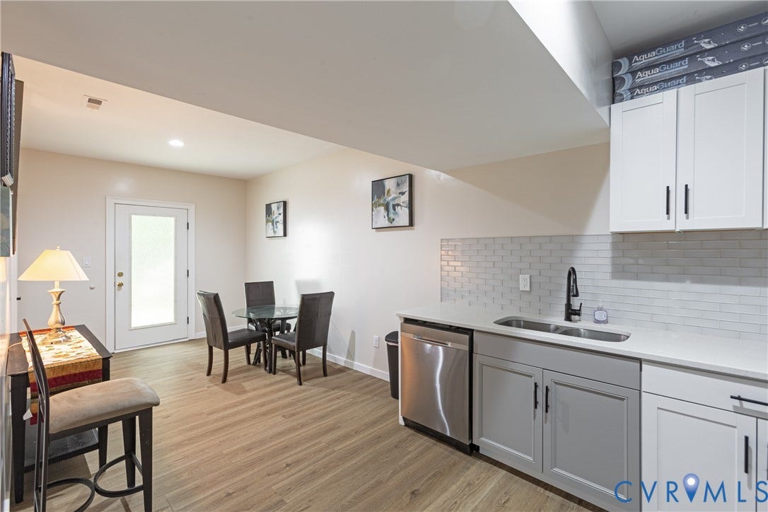 12554 Kain Road, Glen Allen, VA 23059 Modern kitchen and dining area featuring stainless steel appliances, white cabinetry with hardware accents, subway tile backsplash, wood-finish flooring throughout, and a dedicated dining space with seating for multiple guests