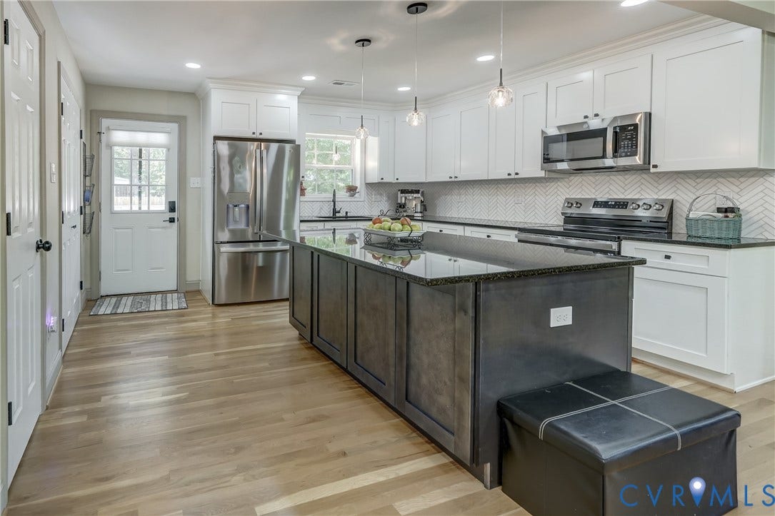 Spacious kitchen featuring an island with a dark countertop, white upper and lower cabinetry, stainless steel appliances, and wood-finish flooring