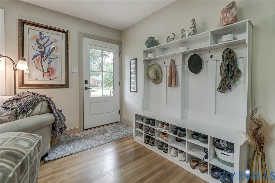 Hardwood flooring, built-in storage bench with shoe cubbies, built-in coat hooks, paneled accent wall, and a glass-paneled exterior door