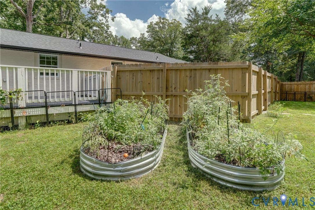 Rear exterior with a wood deck, horizontal railing, and two corrugated metal raised garden beds
