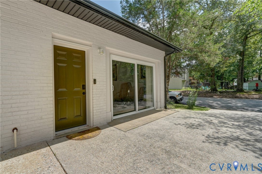 White brick exterior with a green paneled door, sliding glass door, and dark roofline