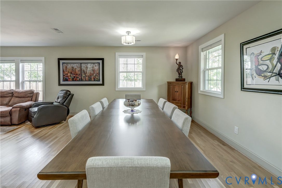 Open-concept living space with light-toned walls, multiple windows, and wood-finish flooring