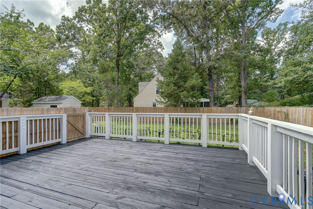 Expansive outdoor deck with dark wood-finish flooring, white railing, and a wood privacy fence