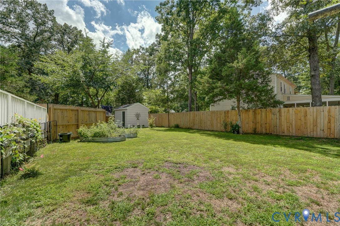 Expansive grassy yard with wood fencing, mature trees, and a storage shed