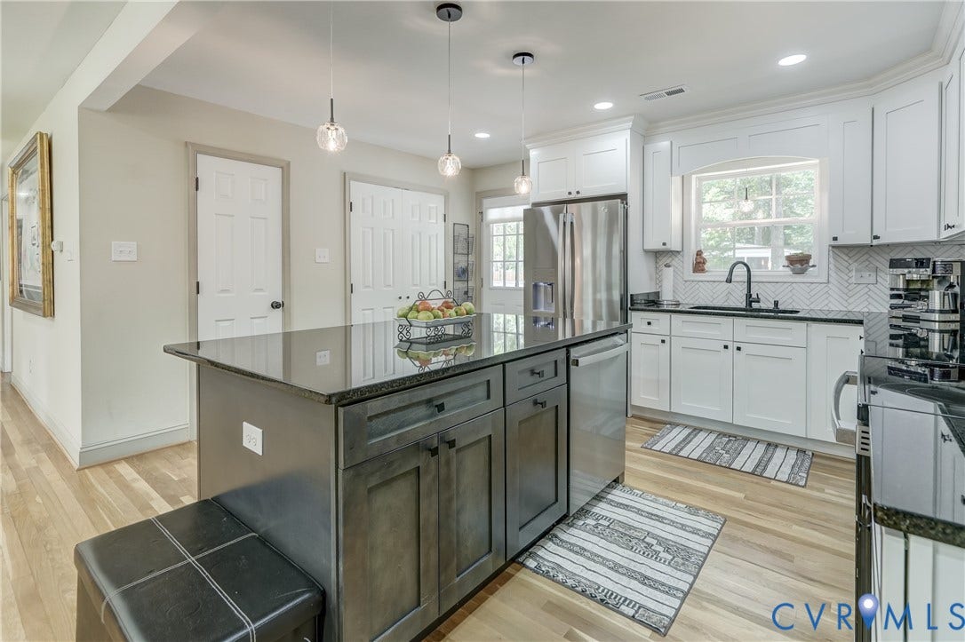 Kitchen featuring a dark-toned island with storage, light wood-finish flooring, white cabinetry, stainless steel appliances, and a dark stone countertop