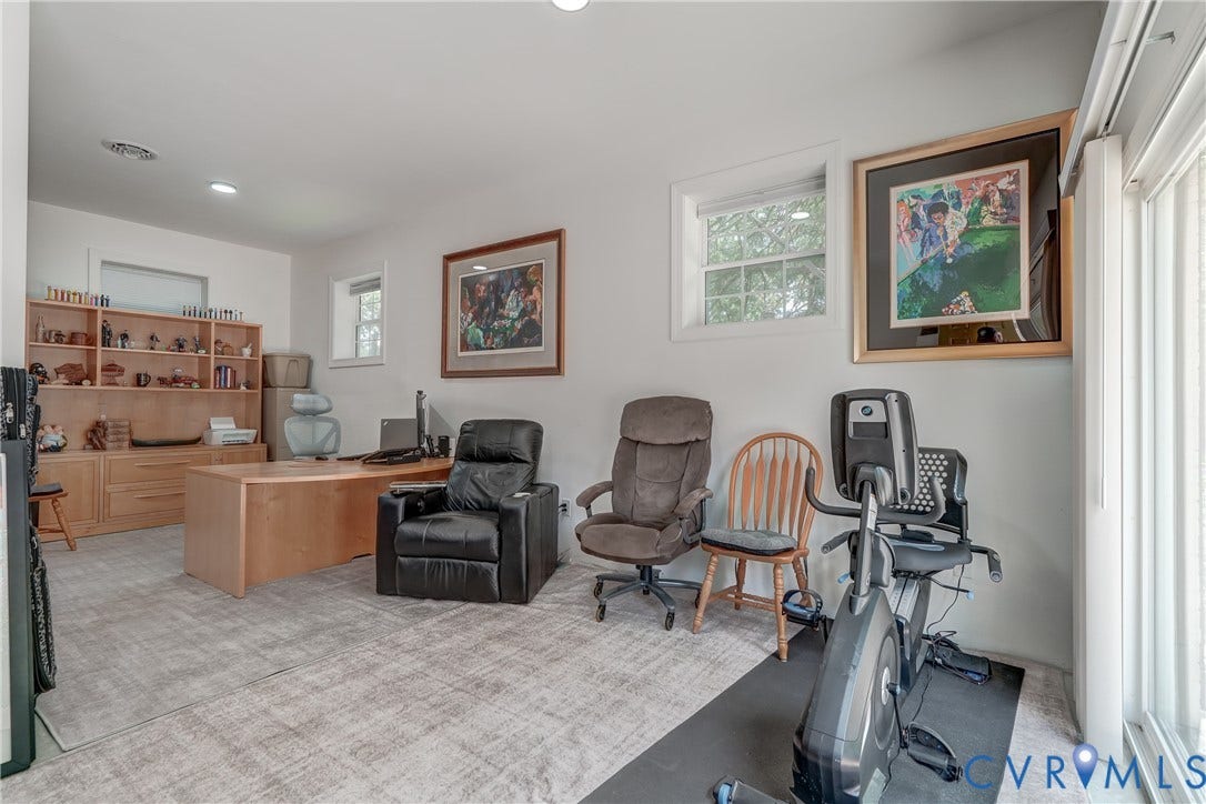 Recessed lighting, wood-finish built-in shelving, wood-finish desk, white window trim, and light-toned carpet flooring