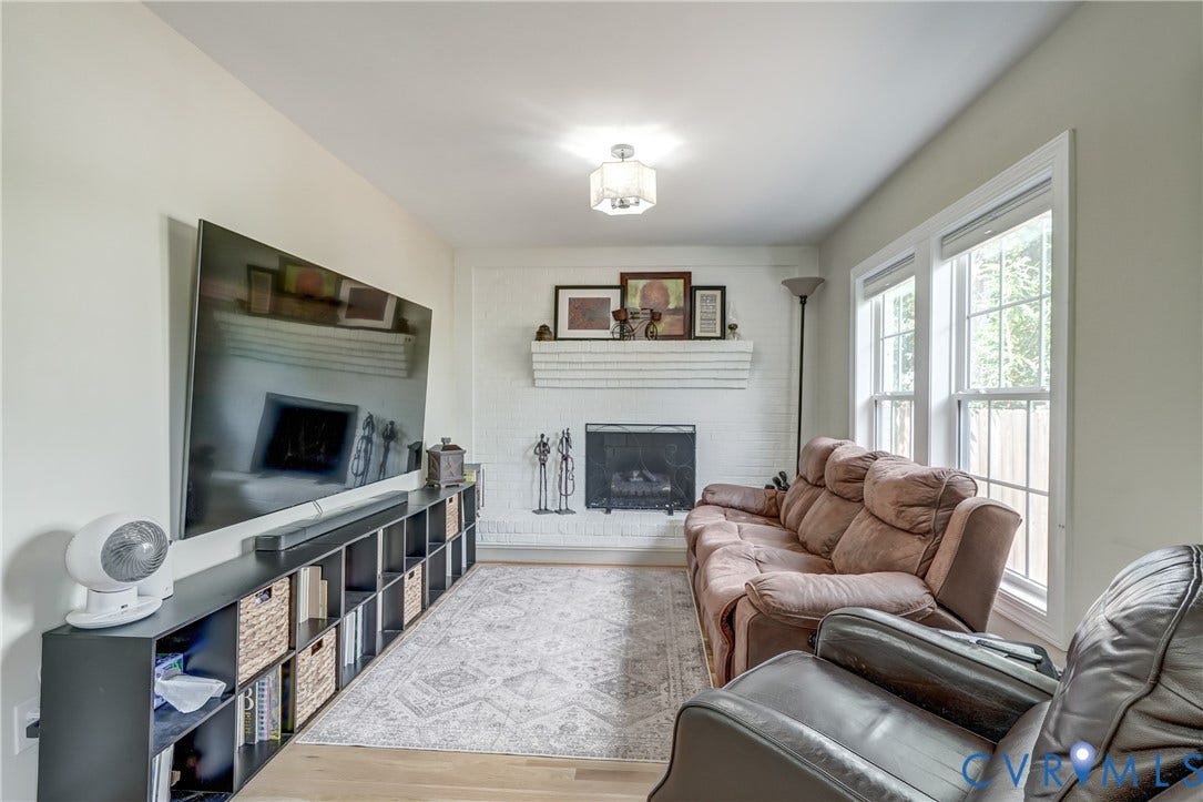 Living area featuring wood-finish flooring, a white brick fireplace with a mantel, and dual windows with white trim