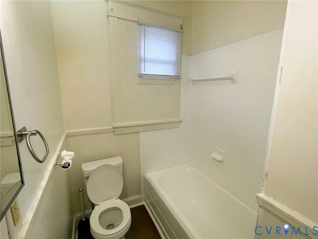 Bathroom featuring a white bathtub, toilet, and window with blinds