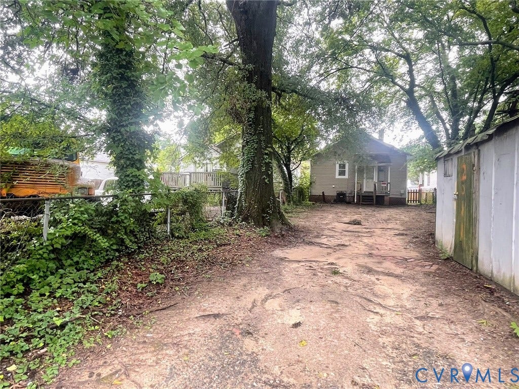 Rear exterior featuring a detached storage shed, chain-link fencing, and mature trees providing natural canopy