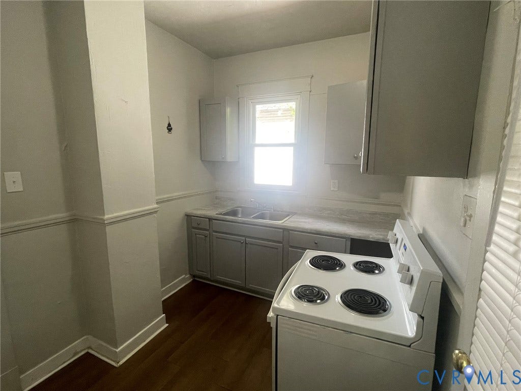 Kitchen featuring wood-finish flooring, white walls with wainscoting, gray cabinetry, a double basin sink, and a white electric range