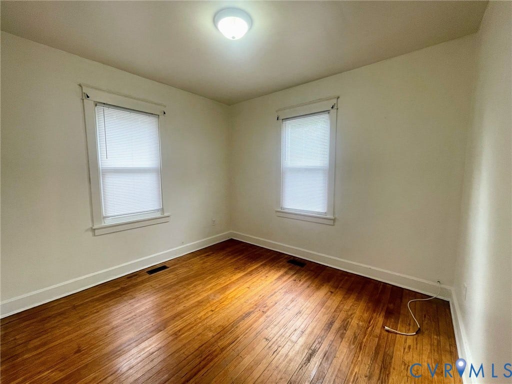 Room featuring wood-finish flooring, two windows with blinds, white trim, and a flush-mount ceiling light fixture