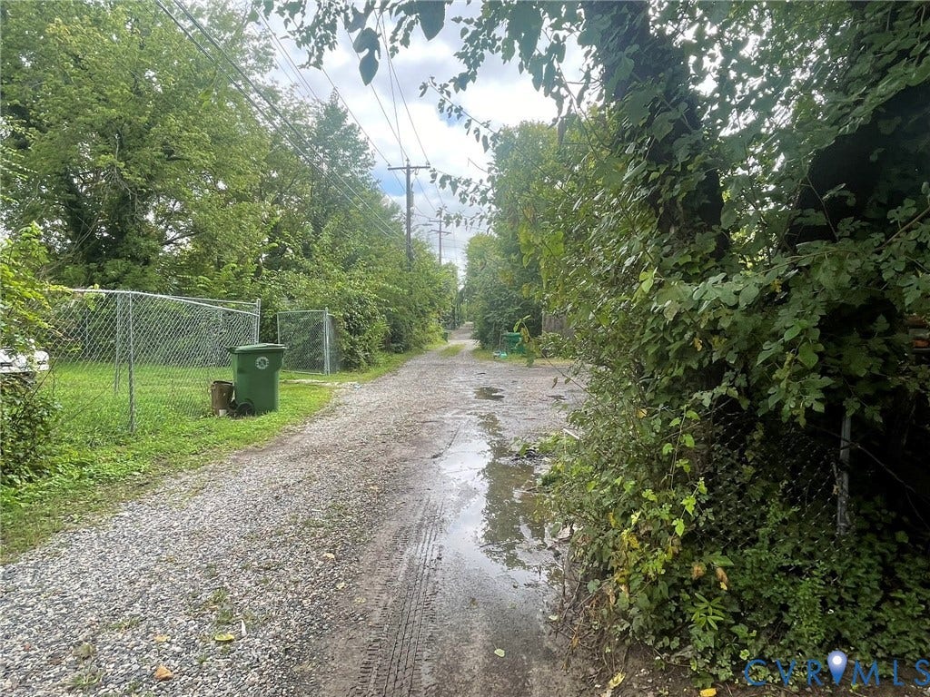 Gravel pathway bordered by mature trees and chain-link fencing