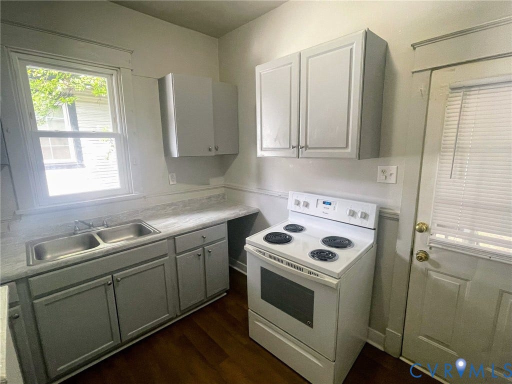 Compact kitchen featuring a double basin stainless steel sink, white electric range, wood-finish flooring, light gray cabinetry, and a window with natural light