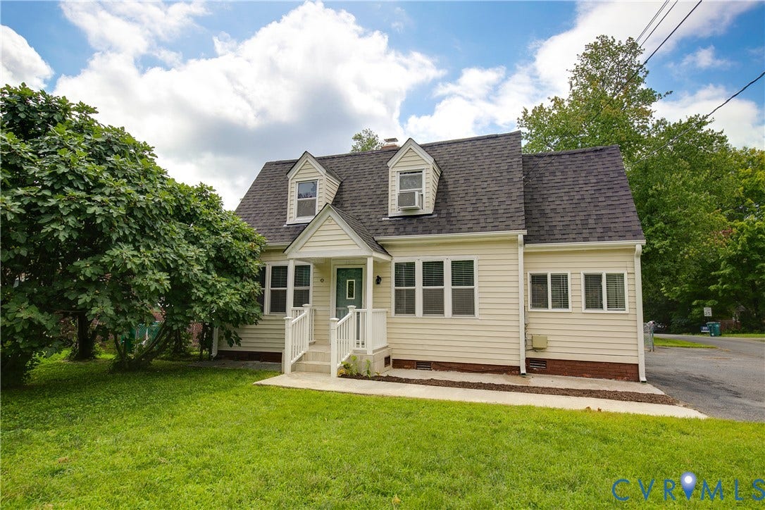 4809 Penick Road, Brookland, Henrico, VA 23228 Classic Cape Cod-style home featuring cream-colored vinyl siding, a steeply pitched asphalt shingle roof with two front-facing dormers, and black shutters flanking multi-pane double-hung windows