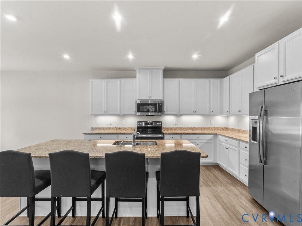 12601 Prestonfield Drive, Blalock, Chesterfield, VA 23836 Kitchen featuring an expansive island with a built-in sink, stainless steel appliances, white cabinetry, and wood-finish flooring