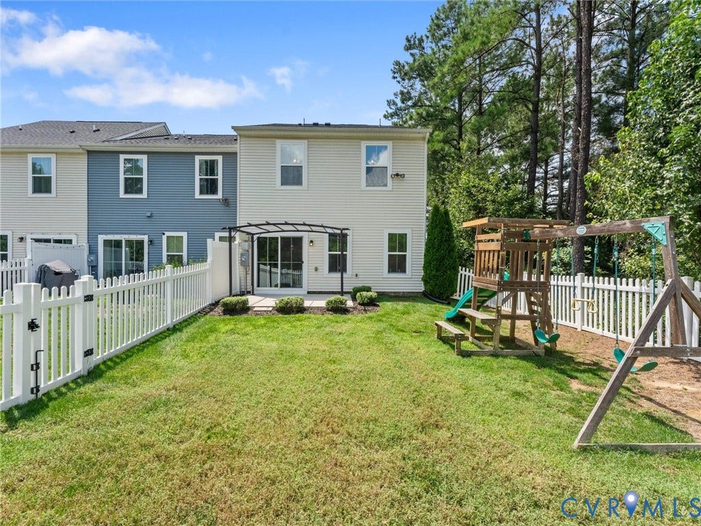 12601 Prestonfield Drive, Blalock, Chesterfield, VA 23836 Expansive backyard with a manicured lawn, white picket fencing, and a stone patio featuring a black pergola
