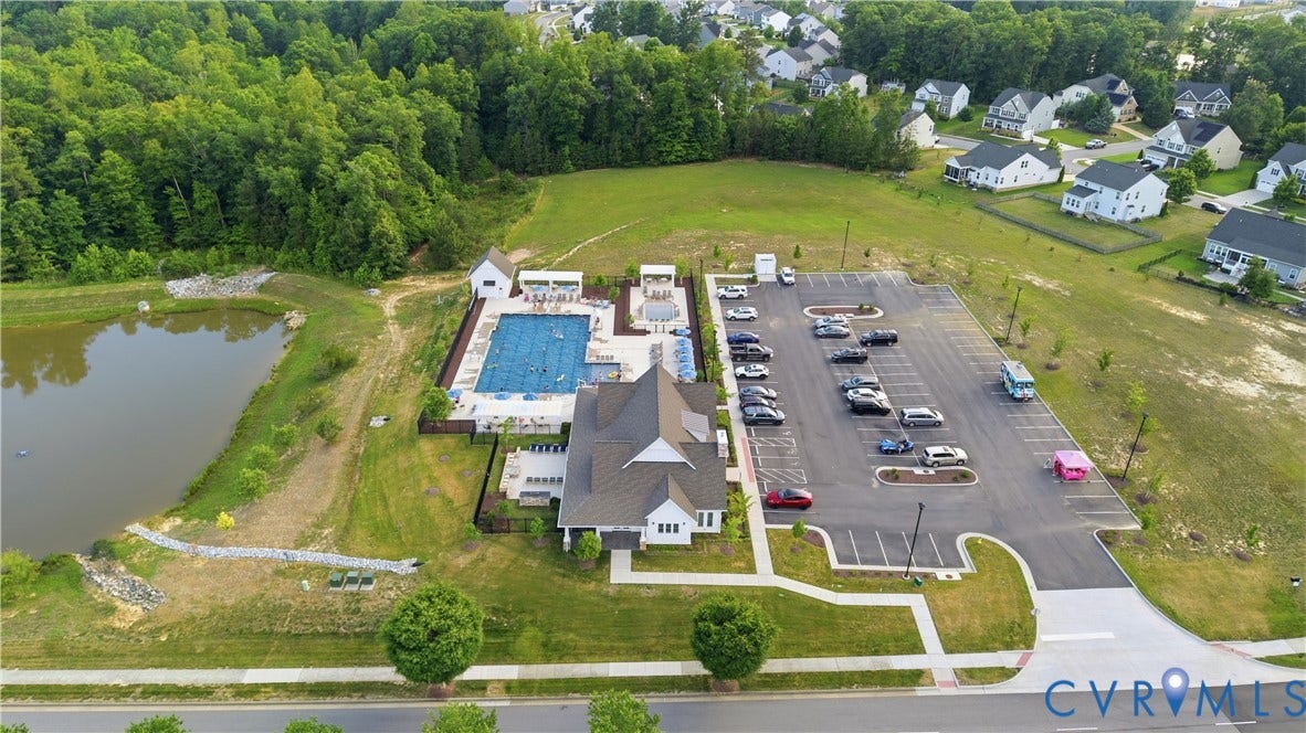Community clubhouse featuring a gabled roofline, a large swimming pool with integrated lounge areas, and a spacious paved parking lot