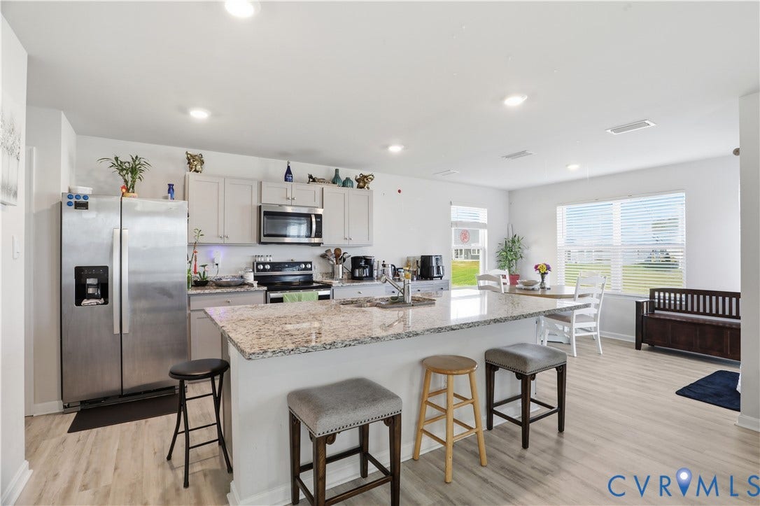 Open-concept kitchen featuring an island with stone-finish countertop, light wood-finish flooring, recessed lighting, and stainless steel appliances