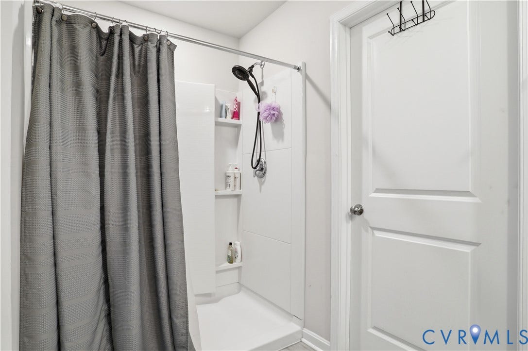 Shower enclosure with white surround paneling, integrated shelving, and a dark-finish showerhead