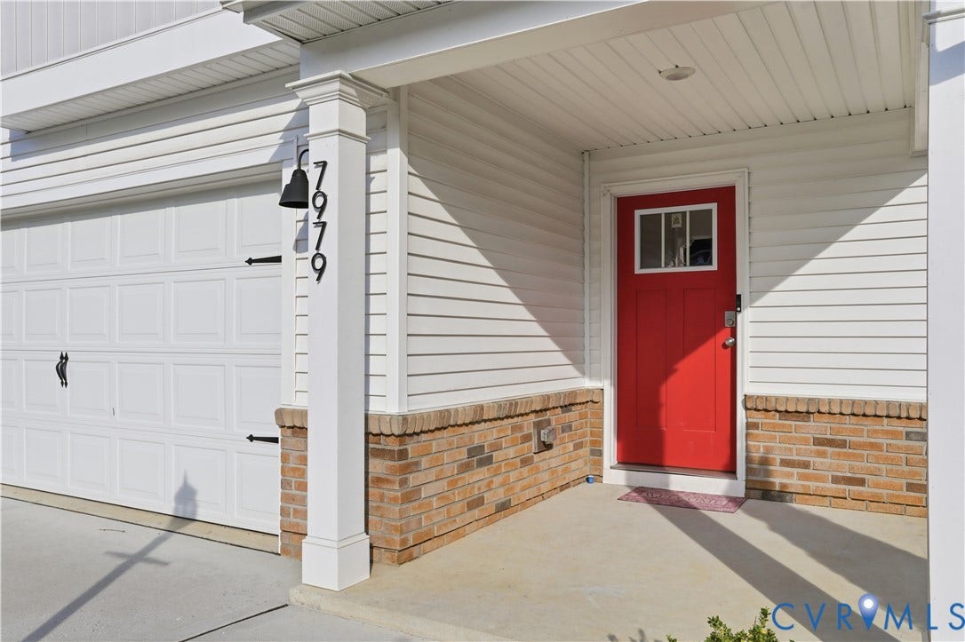 Inviting red front door with upper window pane, white siding, and brick foundation