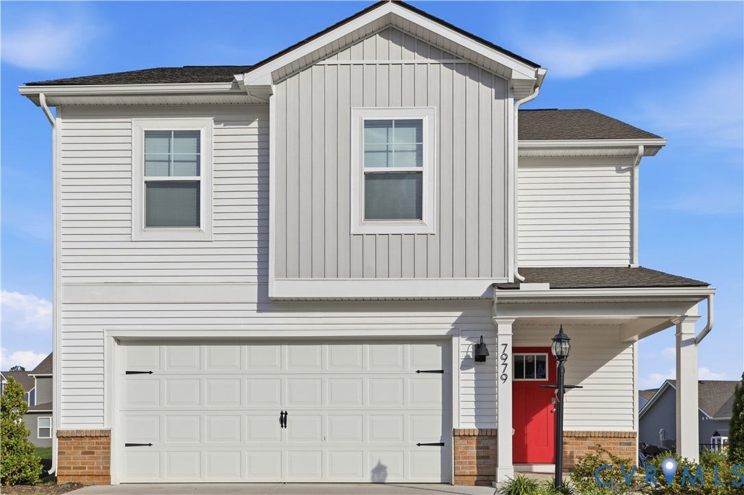 Two-story exterior featuring a prominent red entry door, an integrated two-car garage, mixed siding materials, and a covered porch