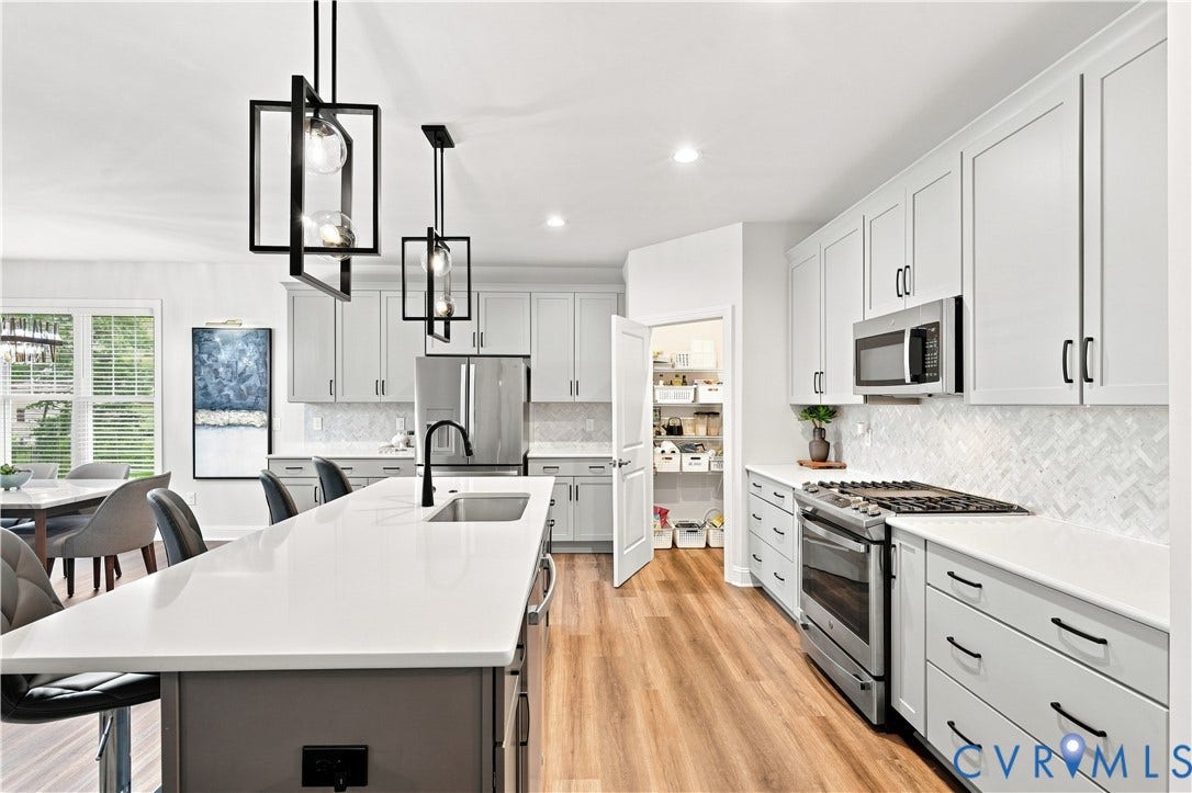 7437 Aldeby Street, Glen Allen, VA 23059 Kitchen featuring an expansive island with a sink, stainless steel appliances, abundant cabinetry, a walk-in pantry, and wood-finish flooring