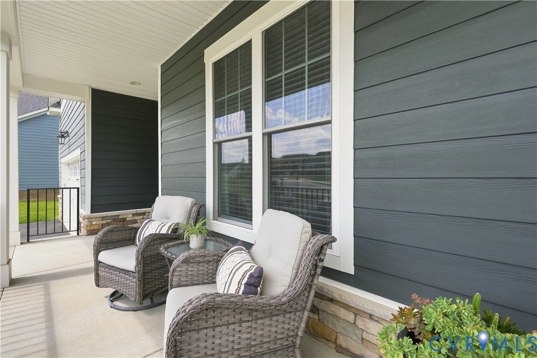 7437 Aldeby Street, Glen Allen, VA 23059 Covered front porch featuring stacked stone accents, dark gray horizontal siding, and a bright yellow paneled entry door with transom and sidelight windows