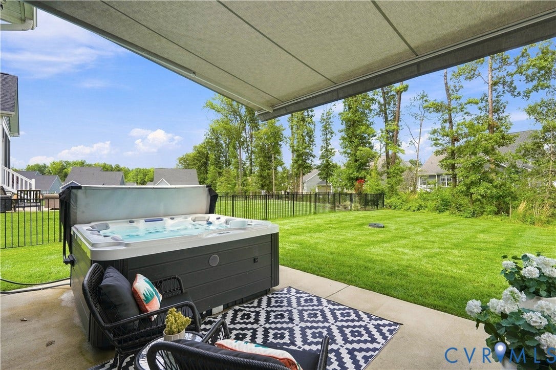 7437 Aldeby Street, Glen Allen, VA 23059 Patio with built-in hot tub / spa, expansive manicured lawn, partial black metal fencing, and mature trees