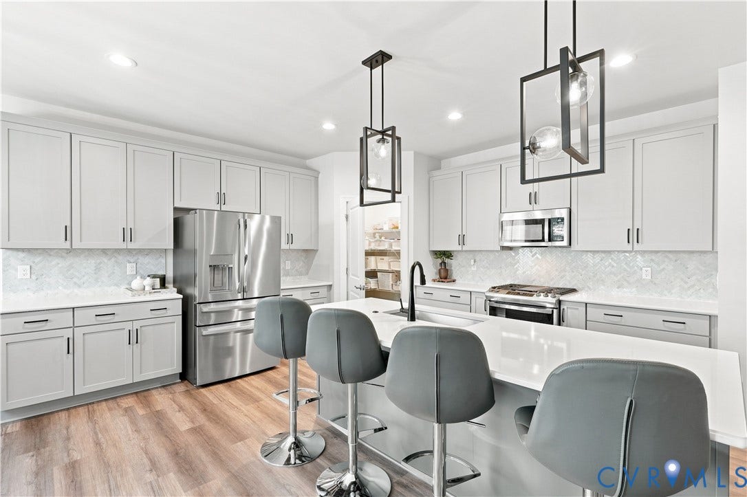 7437 Aldeby Street, Glen Allen, VA 23059 Contemporary kitchen featuring an expansive island, stainless steel appliances, a herringbone tile backsplash, wood-finish flooring, and pendant lighting