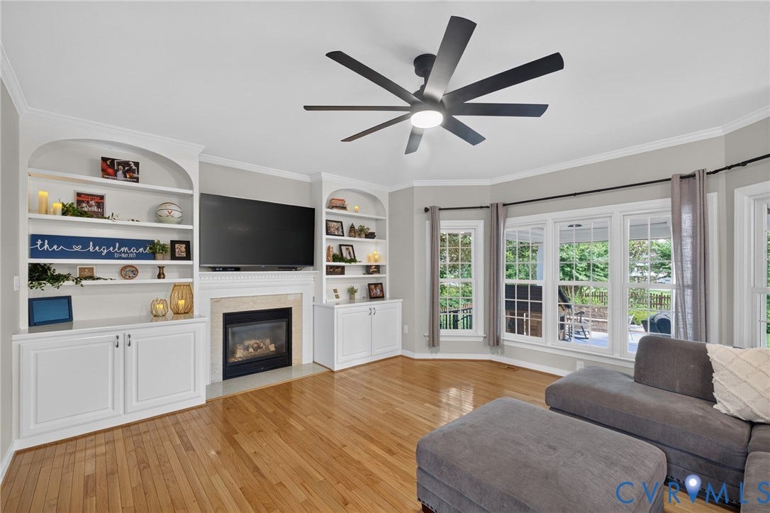 12320 Bradford Landing Way, Glen Allen, VA 23059 Living area featuring hardwood-finish flooring, a built-in fireplace with stone surround, custom white built-in shelving, a modern ceiling fan, and a bay window with multiple double-hung windows