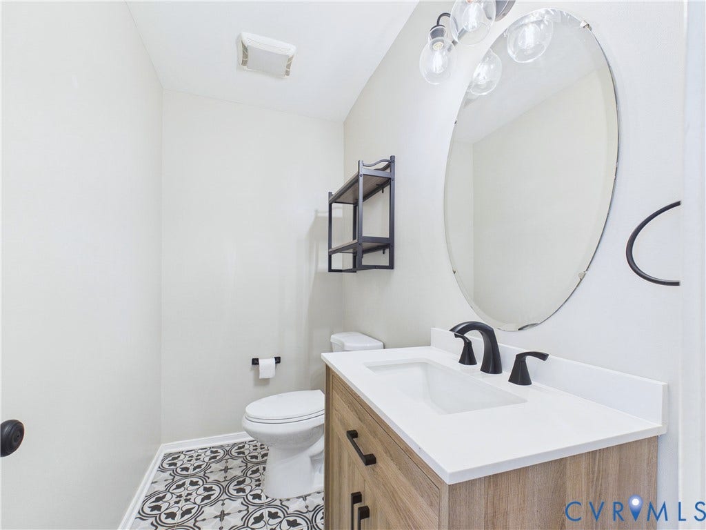 4515 Exton Lane, Chester, VA 23831 Vanity with white countertop and integrated sink, matte black faucet, wood-finish cabinetry, and an oval mirror with a decorative light fixture